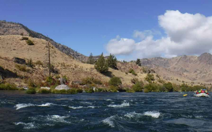 a raft full of people navigates a river under blue skies with clouds 